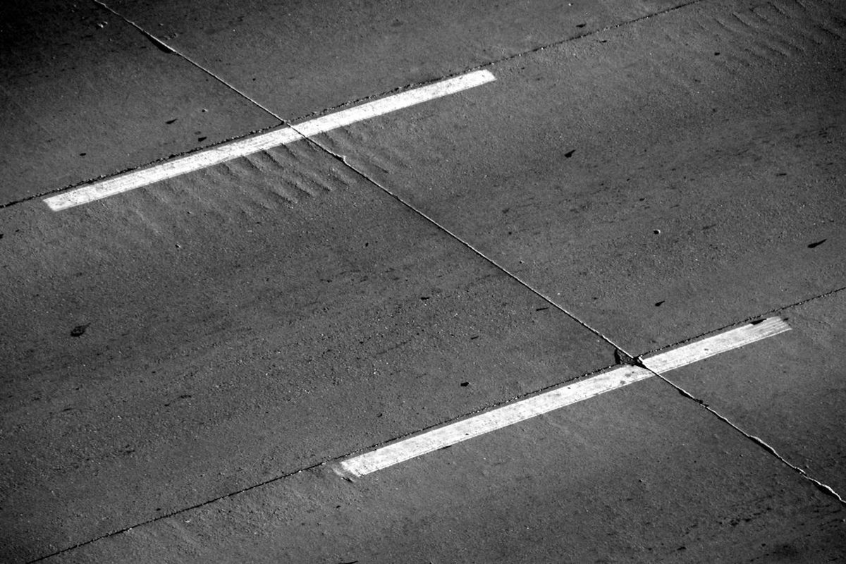 Grieta diagonal en el pavimento que cruza entre dos franjas de pintura blanca paralelas, conectando un punto de la línea superior con uno de la inferior en un solo trazo recto: la misma anatomía de un slope graph, un único segmento diagonal que une el valor de una categoría entre dos momentos distintos
